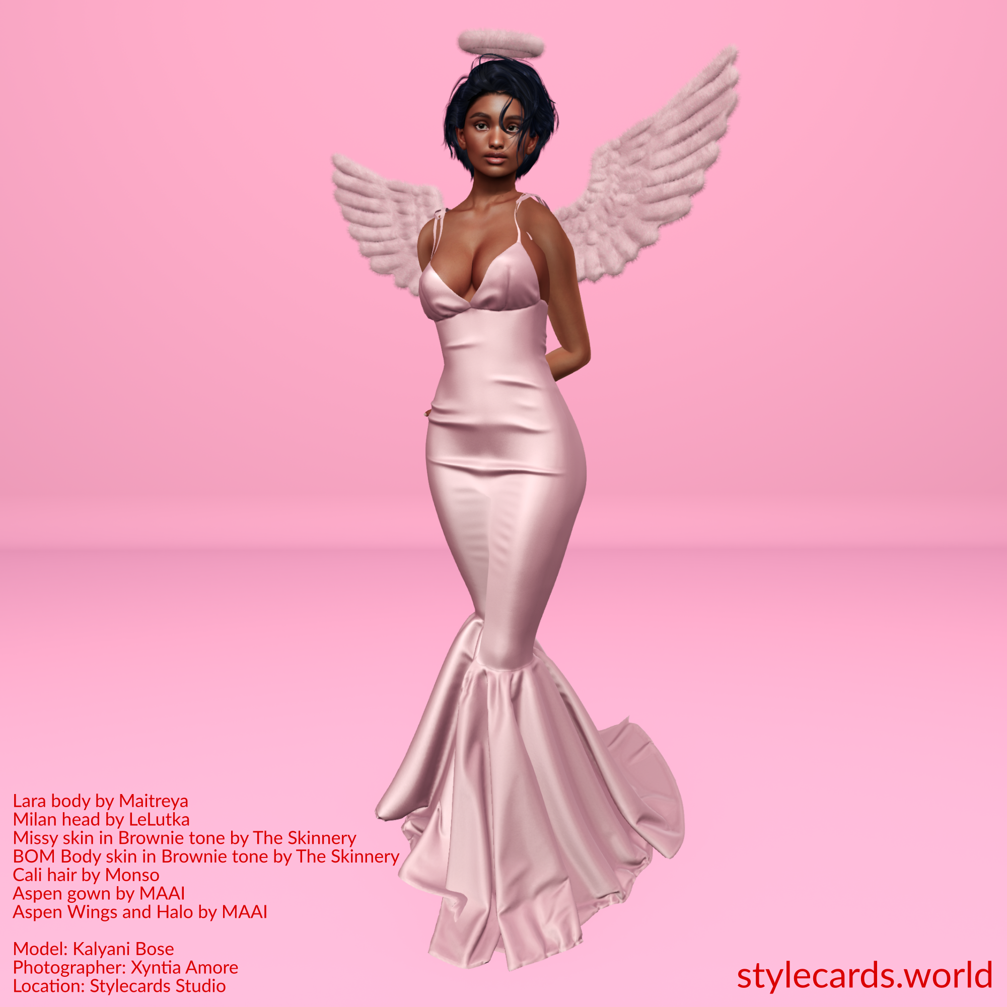 Kalyani Bose is dressed in a pink satin floor-length gown accessorized by a pink halo and angel wings while standing n front of a pink studio backdrop.