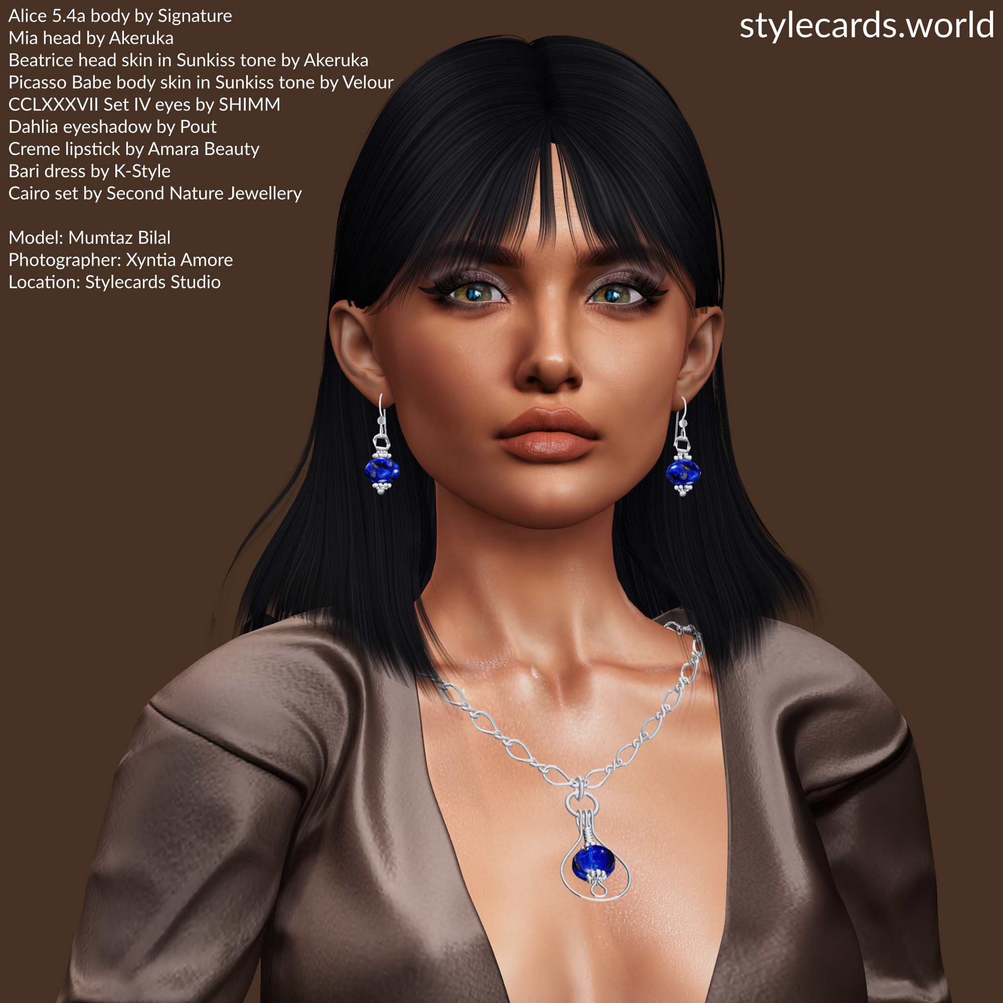 A headshot of Mumtaz Bilal, who is wearing a brown dress and standing in front of a brown backdrop. The photo is accented by the Cairo set of jewelry from Second Nature Jewellery which features vibrant blue gems set in silver.